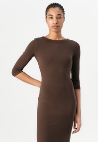 Brown ribbed knit dress with three-quarter sleeves, fitted silhouette, and boat neckline. Smooth texture and form-fitting design.