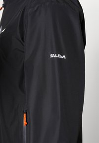 Veste noire avec détail de zipper orange et logo blanc "SALEWA" sur la manche. Fabriquée à partir d'un matériau lisse et léger avec une coupe ajustée.
