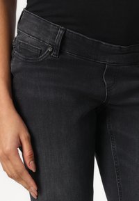 Svarte denimjeans med mid-rise liv, med fem lommer, subtil søm og en jevn tekstur. Tøyet virker slitesterkt.