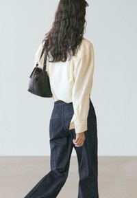 Hellgelbes Langarmhemd kombiniert mit dunkelblauen Denim-Hosen. Das Outfit hat eine lockere Passform und eine kleine braune Schultertasche.