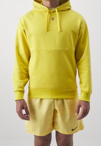 Sweat à capuche jaune avec cordons, comportant un petit logo sur la poitrine. Associé à un short jaune assorti, texture douce et coupe décontractée.