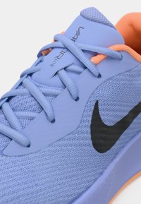 Svetlo modni tekaški čevelj s črnim logotipom, teksturiranim mrežastim zgornjim delom, oranžnimi poudarki in ravnimi vezalkami, z oblazinjeno podplatjo za oporo.