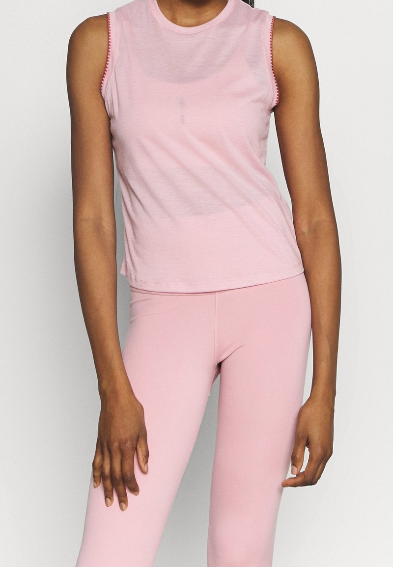 Haut rose pâle sans manches avec un col rond et un bord contrastant. Tissu doux, coupe ajustée et longueur courte. Associé à des leggings assortis.
