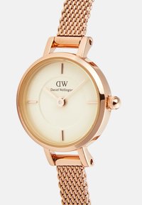 Roségoldene Uhr mit Mesh-Armband und cremefarbenem Zifferblatt, das minimale Stundenmarker und eine einfache Krone zum Einstellen der Zeit aufweist.
