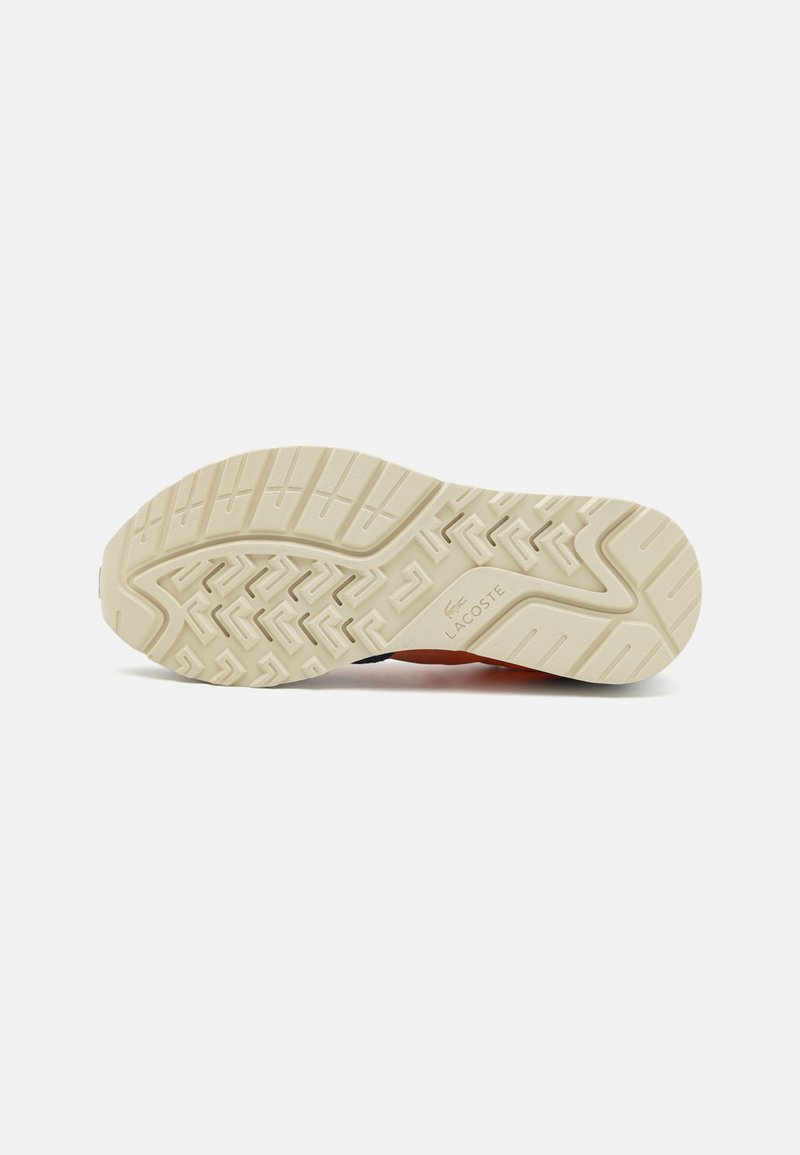Suela de zapatilla Lacoste, de goma color blanco roto con un patrón texturizado y suelas en zigzag. Presenta la marca en el lateral cerca del talón.