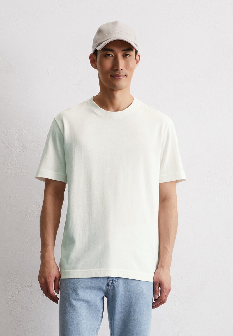 T-shirt en coton vert clair à manches courtes, encolure ras du cou, assorti à un jean en denim bleu clair et une casquette grise claire.