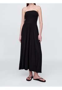 Svart axelbandsfri maxi-klänning i mjukt tyg, med en åtsittande livdel och en flödande kjol. Bärs med svarta flip-flops. Enkel design utan mönster.