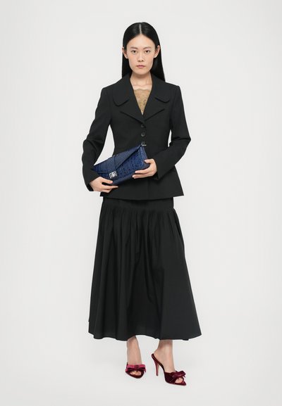 Black tailored blazer with a wide collar, paired with a black pleated skirt. Holding a blue textured clutch and wearing burgundy velvet heels.