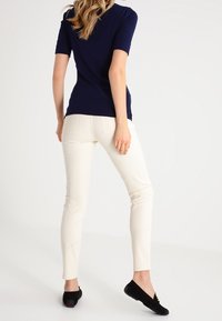 Marinblå kortärmad topp i kombination med krämfärgade snävbyxor och svarta platta skor. Outfiten har en enkel design utan synliga mönster eller detaljer.