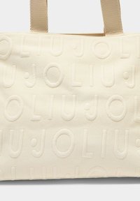 Crèmekleurige draagtas met reliëftekstpatroon van "JOLIU." Voorzien van gestructureerde stof en stevige stoffen bandjes voor gemakkelijk dragen.