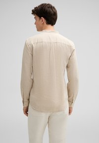 Beige langarmshirt gemaakt van gestructureerde stof, met een bandkraag en knoopmanchetten, gezien van de achterkant.