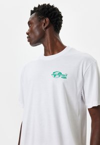 Hvid bomulds t-shirt med rund halsudskæring, korte ærmer, prydet med et grønt grafisk print med "UNBELIEVABLE" og globusdesign på brystet.