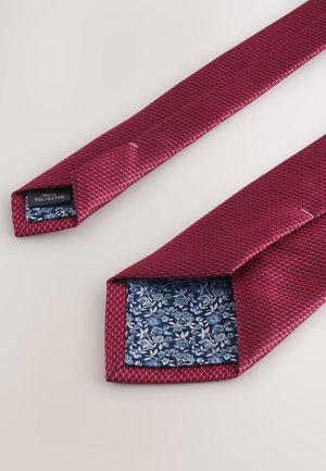 Red textured tie made of 100% polyester, featuring a blue floral-patterned lining visible at the tip. Measures approximately 3 inches wide.