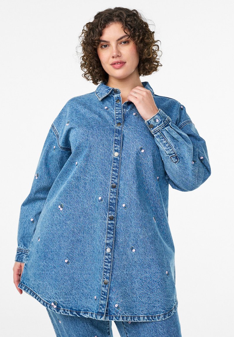 Denim shirt in light blue featuring a button-up front, long sleeves, drop shoulders, and decorative pink flower embellishments throughout.