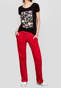 Zwarte t-shirt met korte mouwen en bloemendessin, gecombineerd met losse rode broek en witte sneakers. Casual outfit met een ontspannen pasvorm.