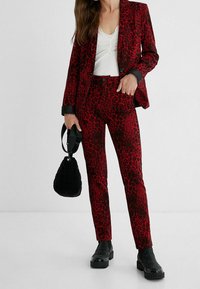 Rood en zwart luipaardprint blazer en bijpassende broek, gecombineerd met een gestructureerde zwarte tas en stevige zwarte laarzen. Slim fit met een gladde afwerking.