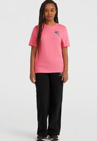 Lyserød bomulds t-shirt med korte ærmer og et grafisk logo, parret med sorte sweatpants med et lille logo nær lommen.