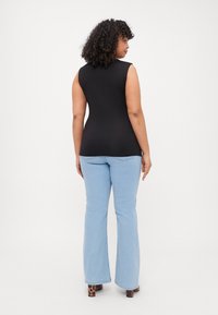 Top sin mangas negro con un diseño ajustado, combinado con jeans acampanados de color azul claro. El modelo lleva unos tacones de bloque con estampado de leopardo.