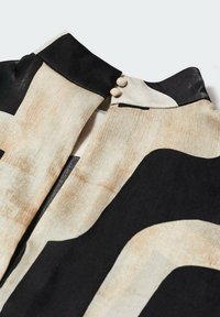 Halenka se černobílým abstraktním vzorem, měkkou tkaninou, vysokým límcem s černým akcentem a dvěma knoflíky u krku.