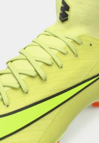 Primer plano de una bota de fútbol amarilla-verde con cordones a juego y un logotipo de Nike en amarillo neón con contorno negro en el lateral.