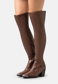 Botas marrones hasta el muslo hechas de cuero sintético con un diseño de estampado de serpiente, que cuentan con una parte superior texturizada, cierre de cremallera y tacón ancho.