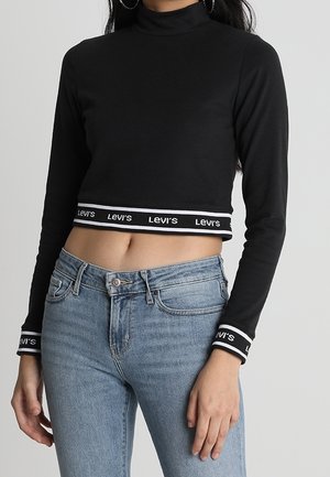 Černý top s dlouhým rukávem, krátký střih, vysoký límec a paspulkou s logem Levi's na lemu a manžetách; nošený s světlými modrými džíny.