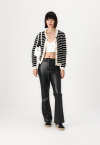 Zwart-witte gestreepte cardigan met crèmekleurige rand, knoopsluiting, gecombineerd met hoge zwarte faux leren broek en zwarte sneakers.