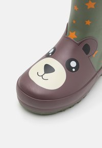 Botte en caoutchouc verte avec un design de visage d'ours brun sur le bout, présentant de grands yeux et un sourire, accentuée par des étoiles orange sur la tige.