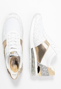 Zapatillas Michael Kors blancas y doradas con tela de malla, detalles estampados y amortiguación transparente en el talón, mostradas desde vistas superiores y laterales.