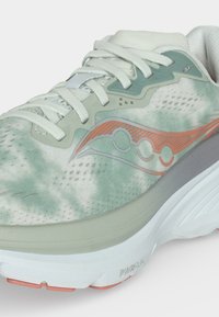 Gros plan sur une chaussure de course blanche et verte avec un logo corail, des lacets blancs et une semelle blanche épaisse étiquetée PWRRUN pour l’amorti.