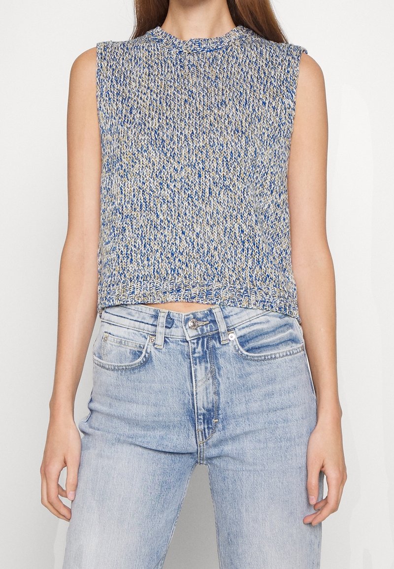 Dzianinowy top bez rękawów w kolorze niebieskim i beżowym, z wysokim kołnierzem i krótkim krojem. Połączony z dżinsami w jasnym odcieniu.