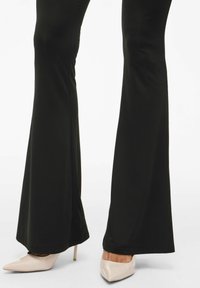 Pantalones acampanados negros hechos de un material elástico, combinados con zapatos de tacón puntiagudos en tono nude con acabado brillante.