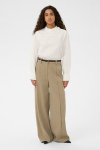 Baltā garā piedurkne blūze ar sakārtotu apkakli un bēšiem augsto jostasvietu platmalu biksēm, papildināta ar melnu ādas jostu un norādītām kurpēm.