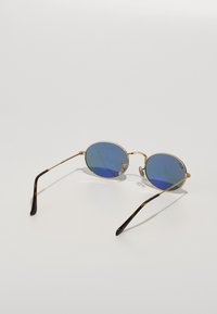 Gafas de sol redondas con lentes de tinte azul, marco de metal dorado y brazos con patrón de carey. Almohadillas nasales transparentes para mayor comodidad.