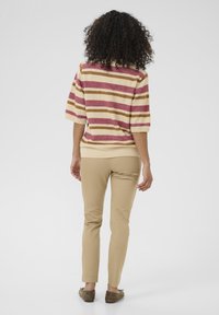 Pruhovaný pletený svetr v béžové, růžové a hnědé barvě, spárovaný s béžovými slim-fit kalhotami. Měkká textura a volný střih, s krátkými rukávy a žebrovanými manžetami.