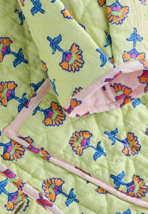 Tissu matelassé en vert clair, avec des motifs floraux orange et rose, et des bords rose pâle. Surface texturée avec des détails de couture.