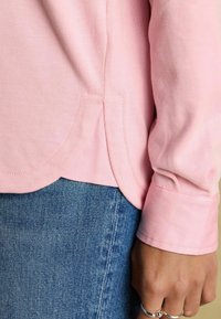 Hele roosa pikkade varrukatega särk, millel on kaarjas hem, sooniktekstuur ning õmmeldud detailid, kombineeritud sinise denimisel materiaalist seelikuga.