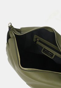 Interno di una borsa in pelle verde oliva con rivestimento nero, zip dorata e tasca interna con zip. Superficie testurizzata e design strutturato.