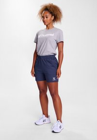 Grå bomullst-shirt med vitt tryck, kombinerad med marinblå shorts med resår i midjan och en liten logotyp på fållen. Vita sportskor.