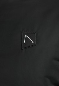 Zwarte stof met een klein zwart patch dat in het midden een witte abstracte hoekige lijnontwerp heeft geborduurd.