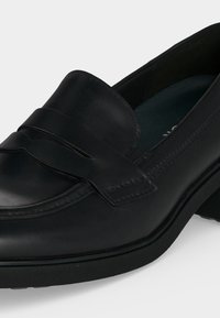 Mocassin en cuir noir avec bout arrondi, talon bas et bride décorative sur le dessus, présenté sur un fond uni.