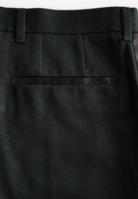Schwarze, strukturierten Hosen mit einem feinen diagonalen Muster. Merkmale umfassen eine schmale Passform, einen glatten Bund und eine Paspeltasche auf der Rückseite.