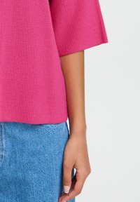 Fuksijasti pleten pulover z rebrasto teksturo in širokimi kratkimi rokavi, v kombinaciji z svetlo modrim jeans krilom.