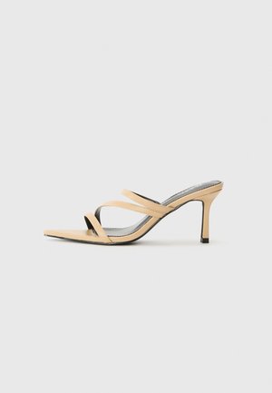Sandálias de salto alto bege com três tiras cruzadas, design de bico fino e um detalhe preto no salto. Material suave e acabamento elegante.