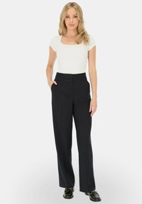 Biała bluzka z krótkim rękawem o kwadratowym dekolcie, zestawiona z szerokimi spodniami w czarne paski. Spodnie mają wysoki stan i boczne kieszenie.