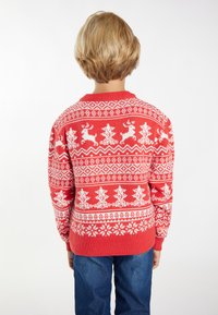 Czerwony sweter robiony na drutach z białymi wzorami reniferów i drzew, z okrągłym dekoltem i długimi rękawami. Noszony przez dziecko z jasnymi włosami.