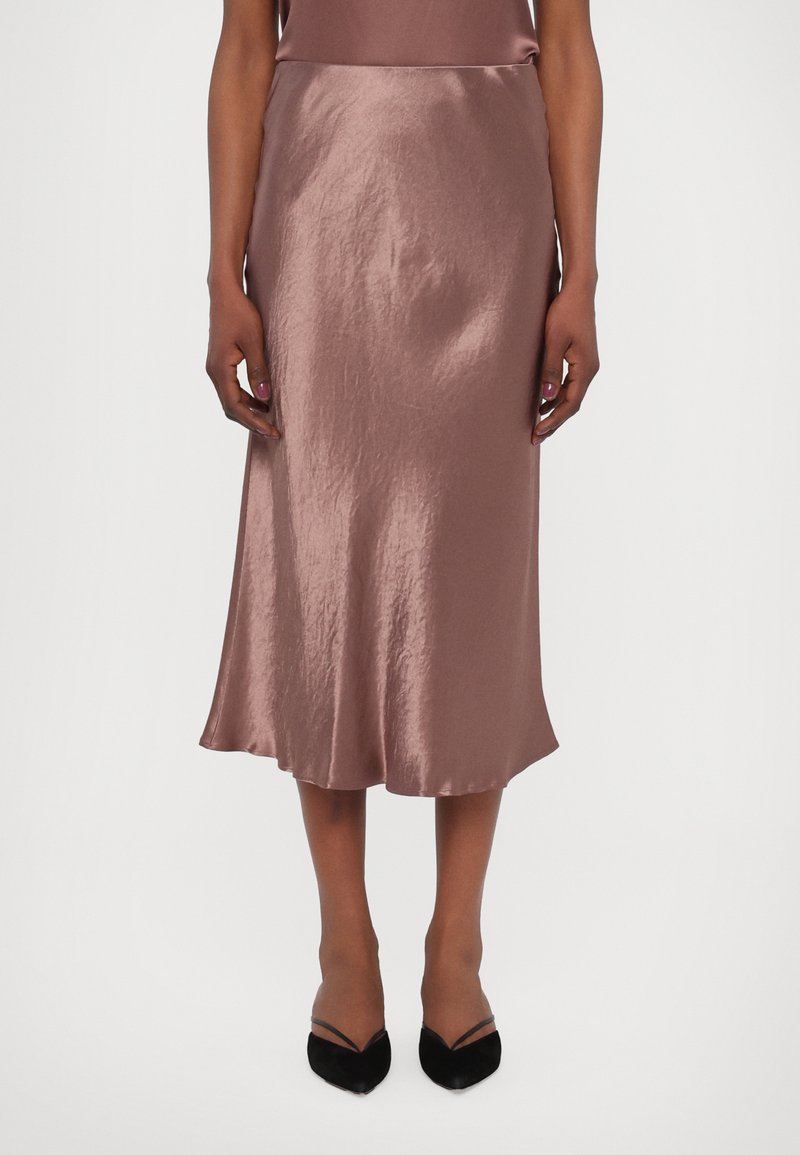 Satin midi skjørt i støvet rosa med en glatt tekstur, som har en utvidet kant og en tettsittende midje. Bært med svarte hæler.