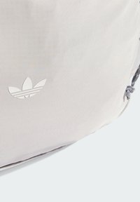 Svetlosivý batoh s textúrovaným látkovým povrchom, ktorý má biele logo adidas a zaväzovanie na šnúrku. Jednoduchý a funkčný dizajn.