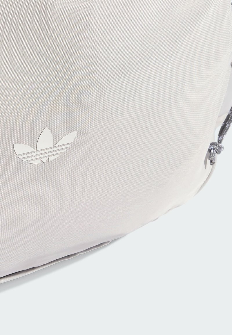 Lysegrå rygsæk med en tekstureret stofflade, der har en hvid adidas-logo og snørelukning. Enkel og funktionel design.