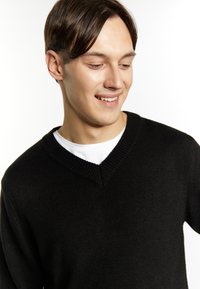 Pulover negru, tricotat, cu un design în formă de V. Purtați peste o cămașă albă cu gât rotund. Textură netedă și detalii fine cu nervuri la guler.